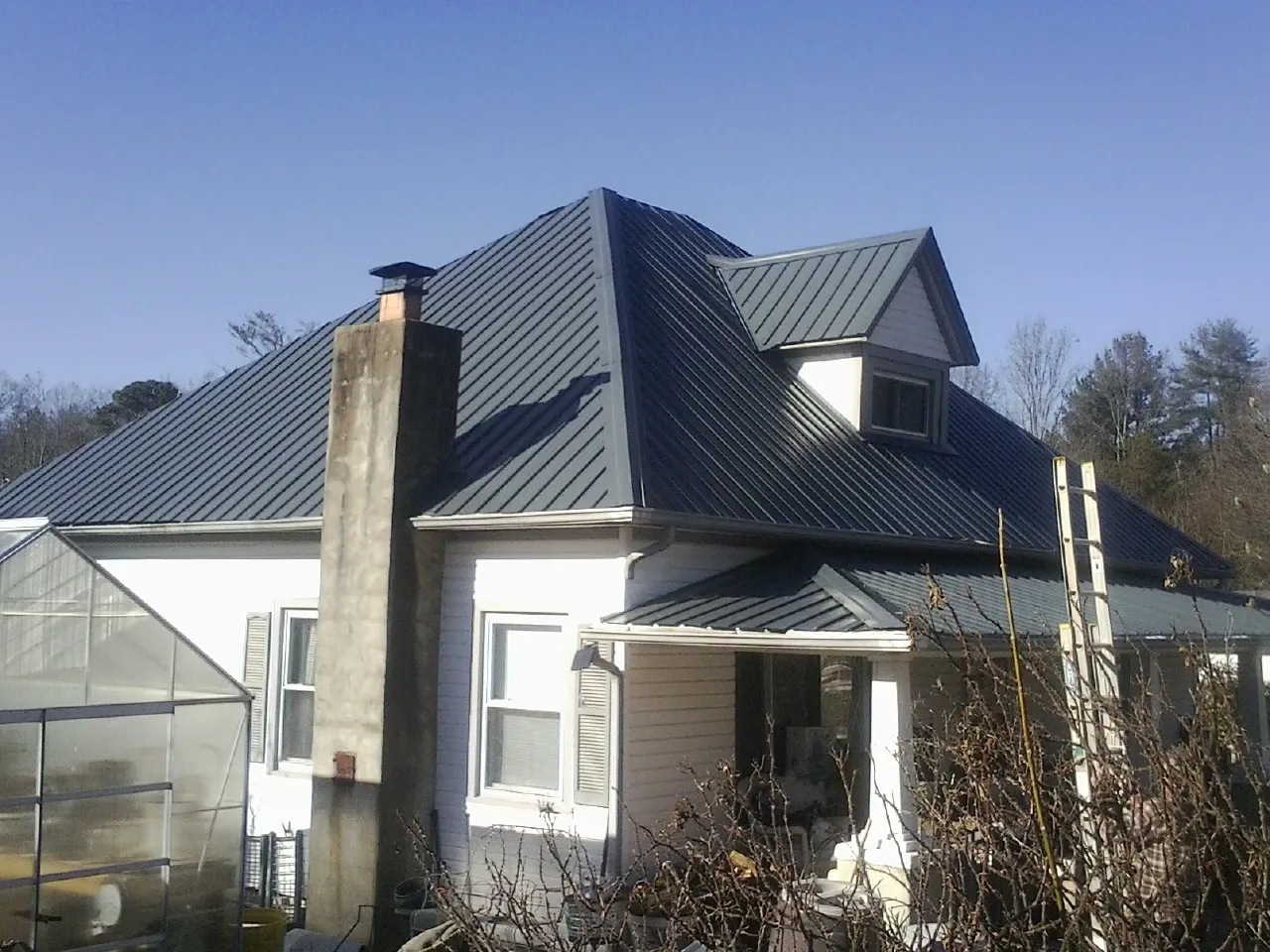 Dark blue standing seam metal roof on a white farmhouse with dormer — Slate & Tile Roof Repair by Roofing Brothers in New River