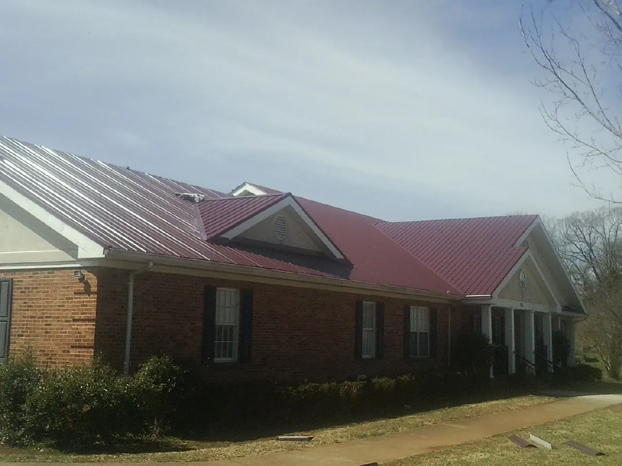 Red metal roof with gabled entries on a long brick building, from a Hail Damage Roof Repair job in New River