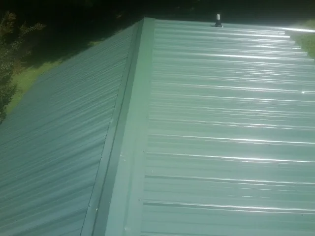 New green metal panels meeting at the ridge of a roof — Flat Roof Repair work by our crew in New River